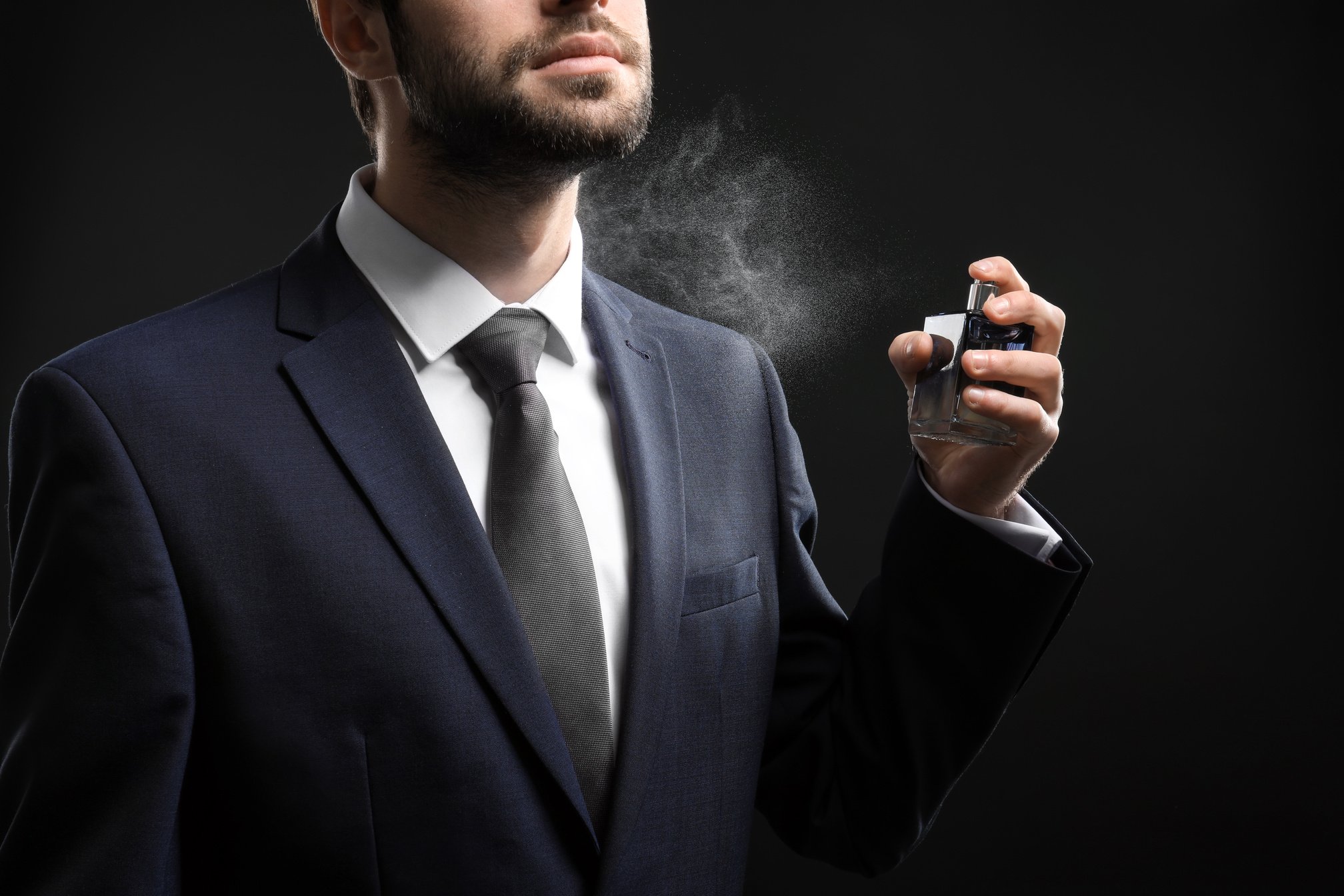 Man in Suit Spraying Perfume Bottle on Black Background